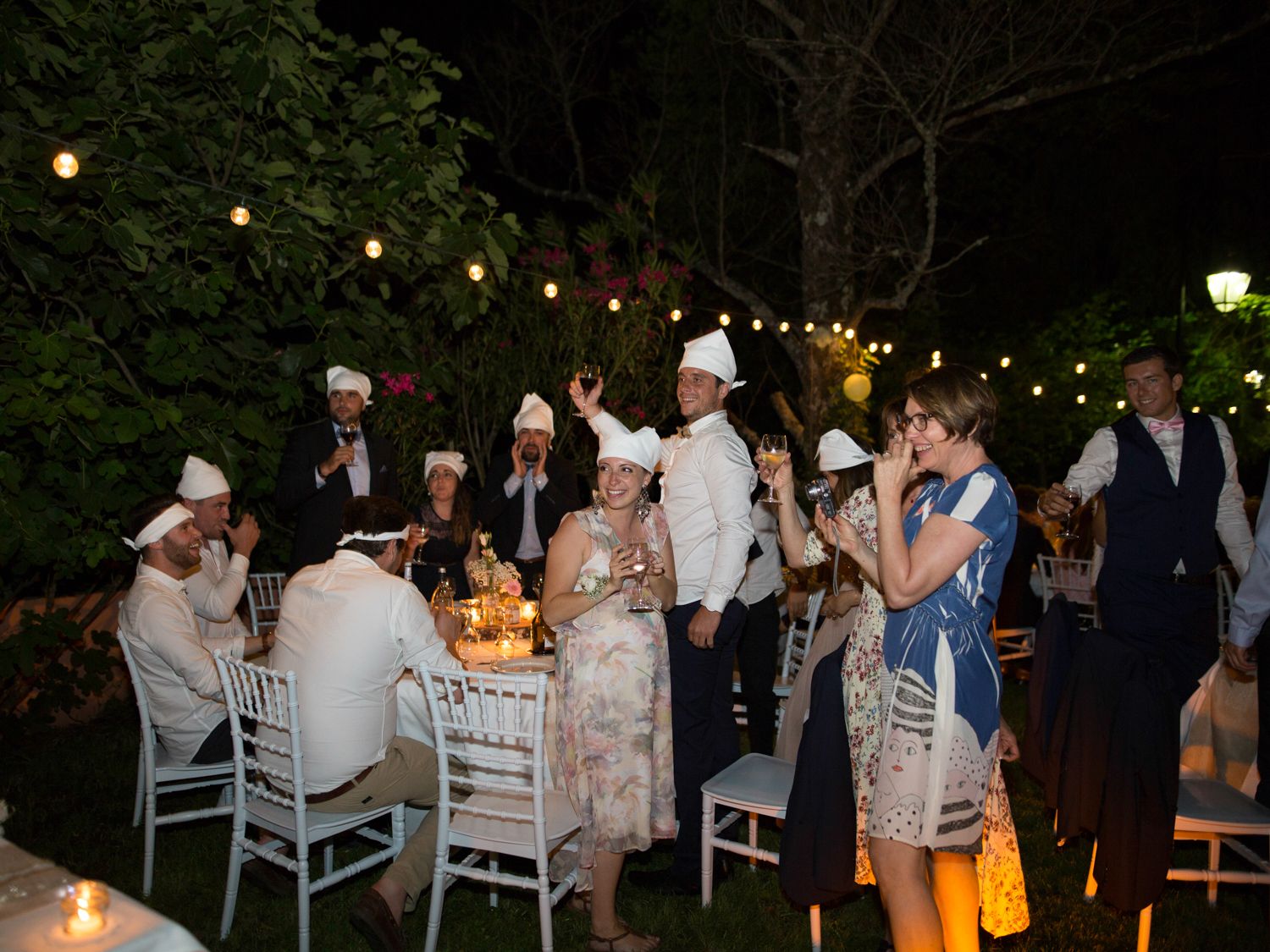 Les invités, coiffés de chapeaux blancs, célèbrent la réception en plein air, éclairée aux chandelles, le soir même.