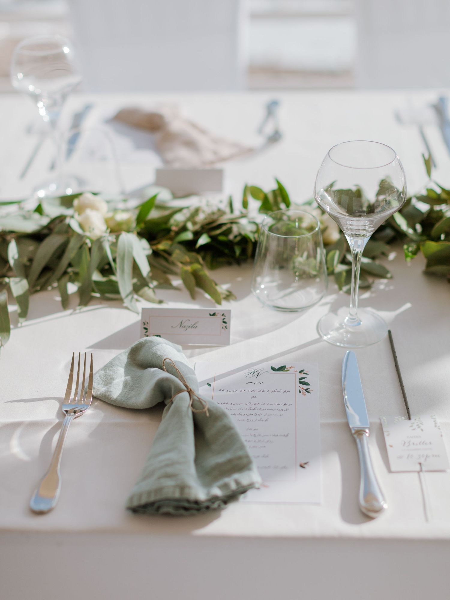 Élégante décoration de table de mariage avec des serviettes vert sauge, des verres en cristal, une guirlande de feuillage