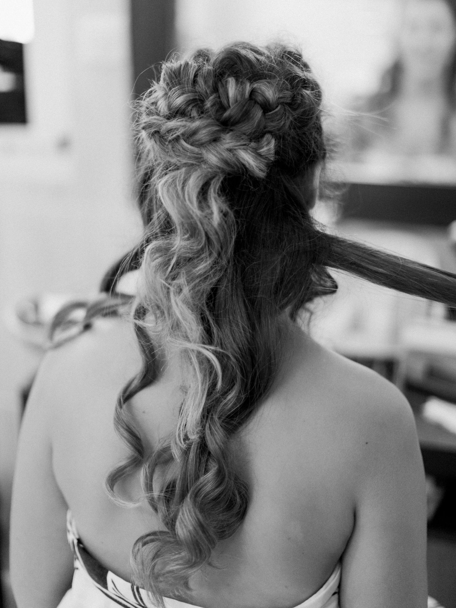 Photo en noir et blanc d'une élégante coiffure de mariée en demi-queue, avec une couronne tressée et des boucles en cascade.