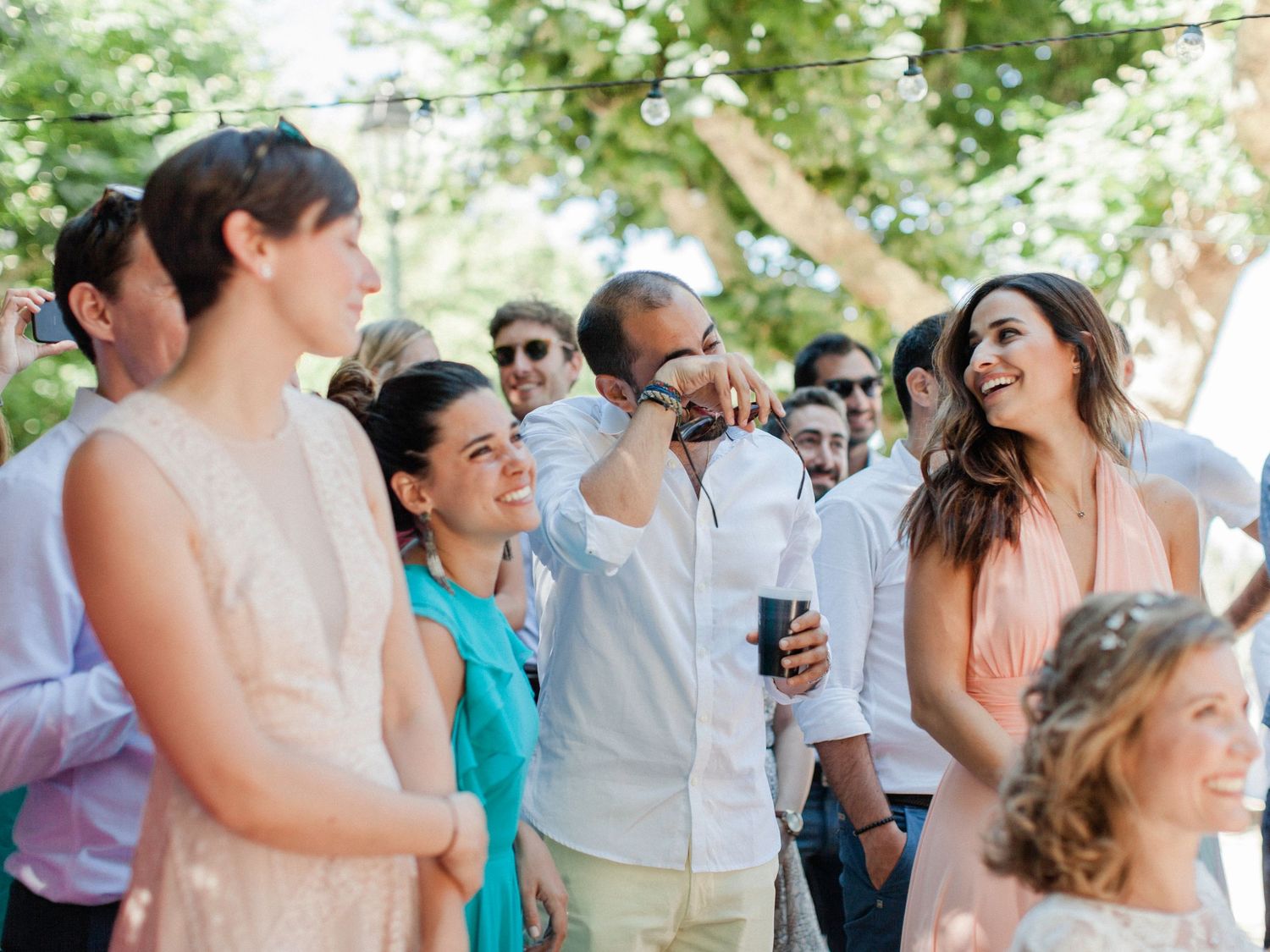 Guests laughing and celebrating outdoors at a summer wedding reception under green trees.