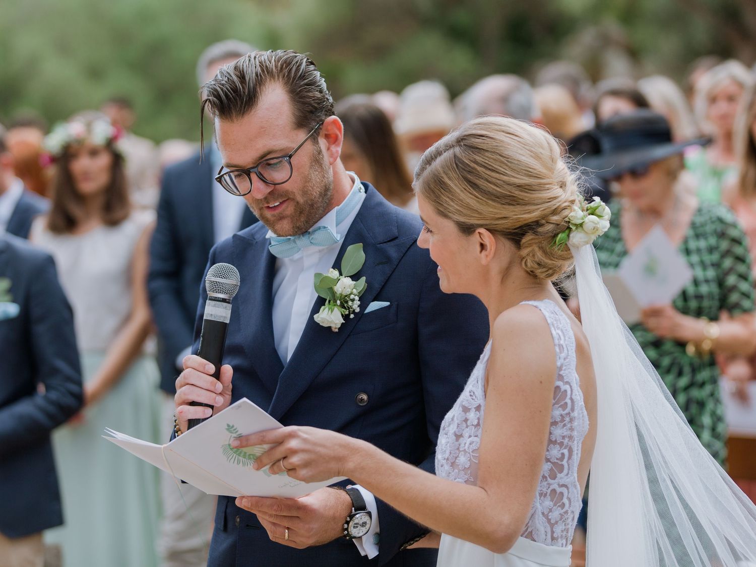 Le marié, en costume bleu marine, lit ses vœux de mariage au micro, à côté de la mariée en robe de dentelle blanche à Bonifacio en corse