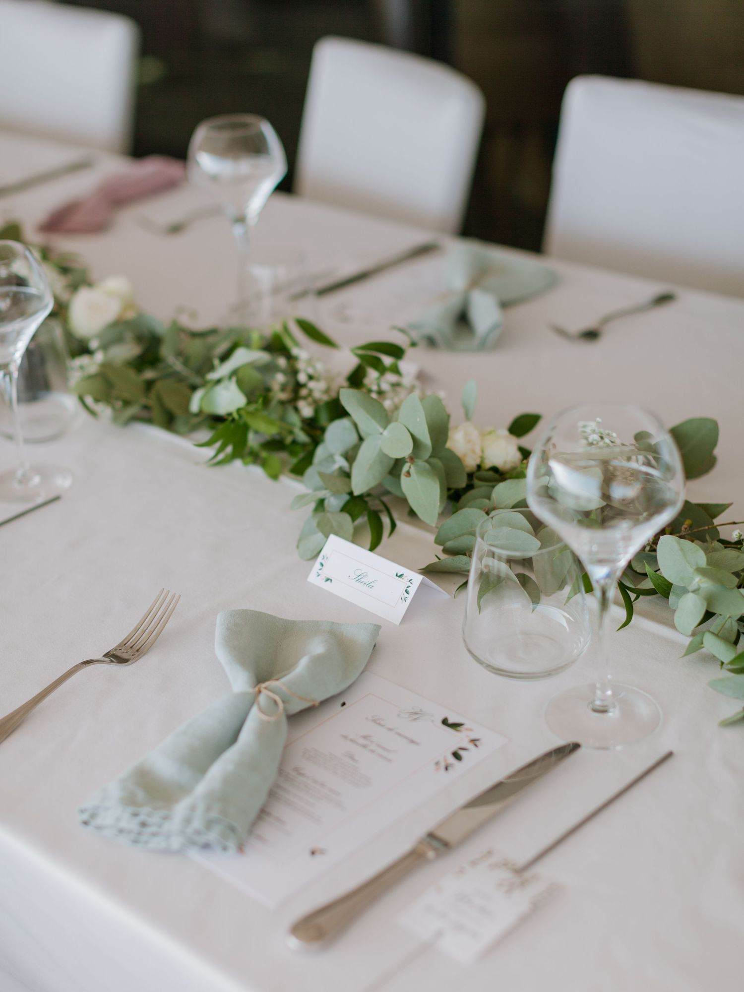 Élégante décoration de table de mariage avec guirlande d'eucalyptus, roses blanches, serviettes vert sauge et verrerie en cristal
