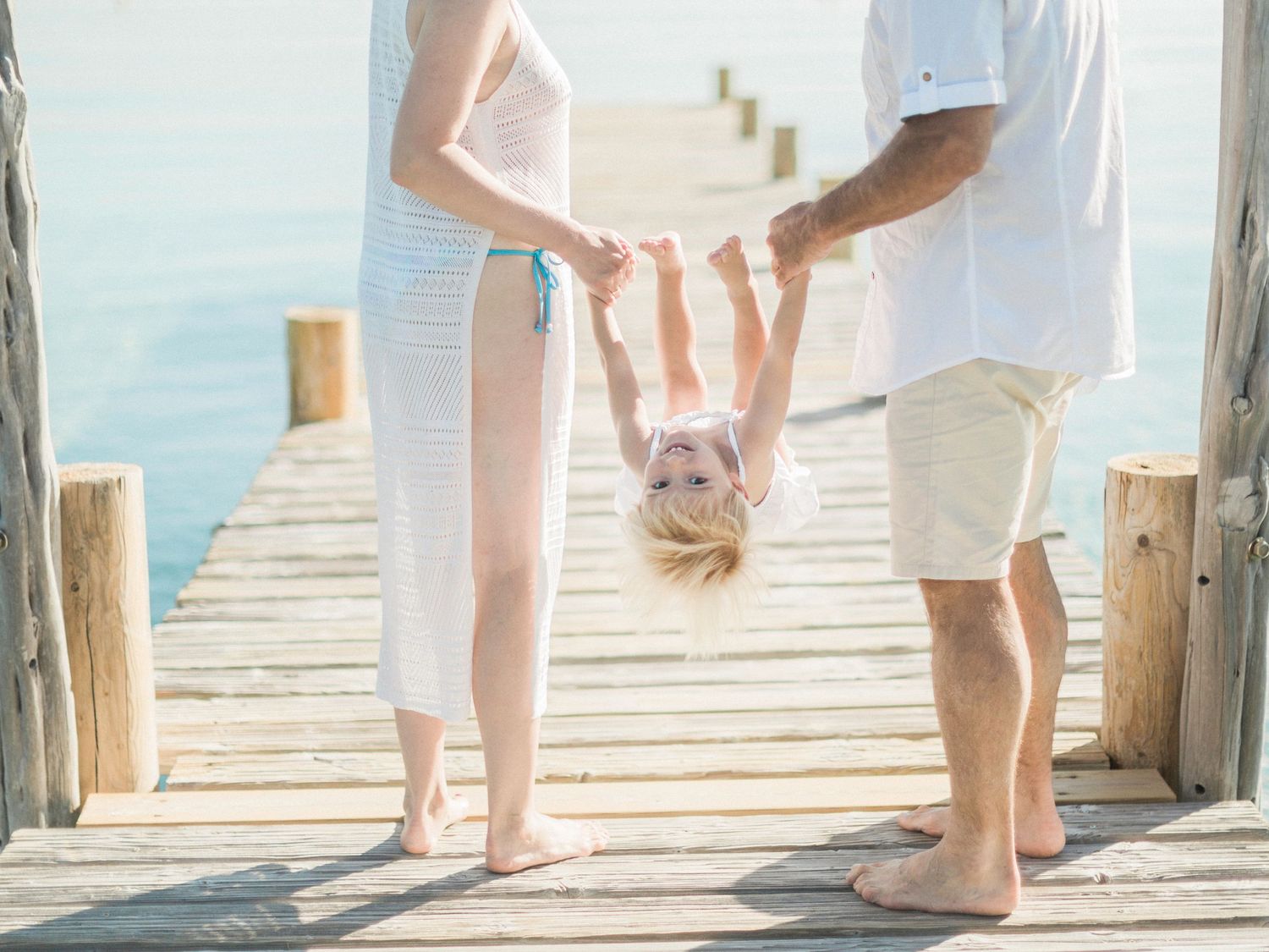Des parents balancent leur tout-petit la tête en bas sur un quai en bois au-dessus d'une eau bleue calme, près de porto-vecchio.