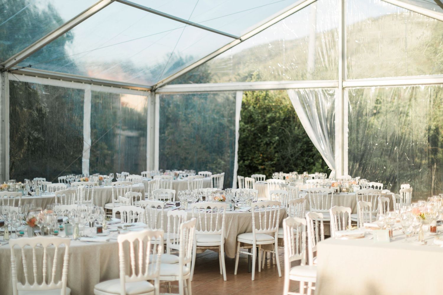 Élégante tente de réception de mariage avec tables rondes blanches,  et plafond en verre transparent à campomoro par le hussard corse