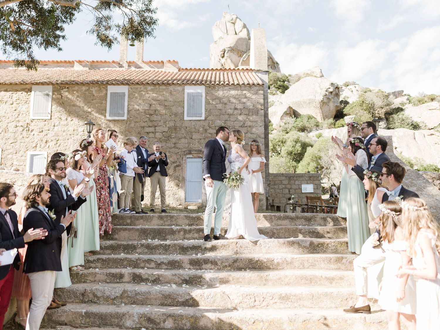 Les jeunes mariés descendent des marches en pierre, entourés d'invités enthousiastes, lors d'une cérémonie champêtre en plein air