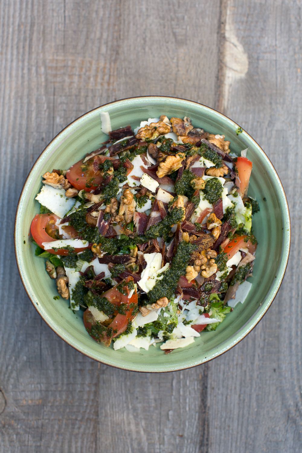 Salade de chou frisé frais avec tomates, noix, fromage et mesclun, servie dans un bol rustique en céramique verte.