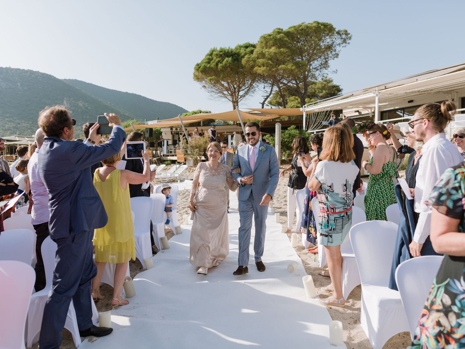 Cérémonie de mariage en plein air où les invités bordent l'allée tandis que le couple s'y avance, dans un cadre méditerranéen ensoleillé.