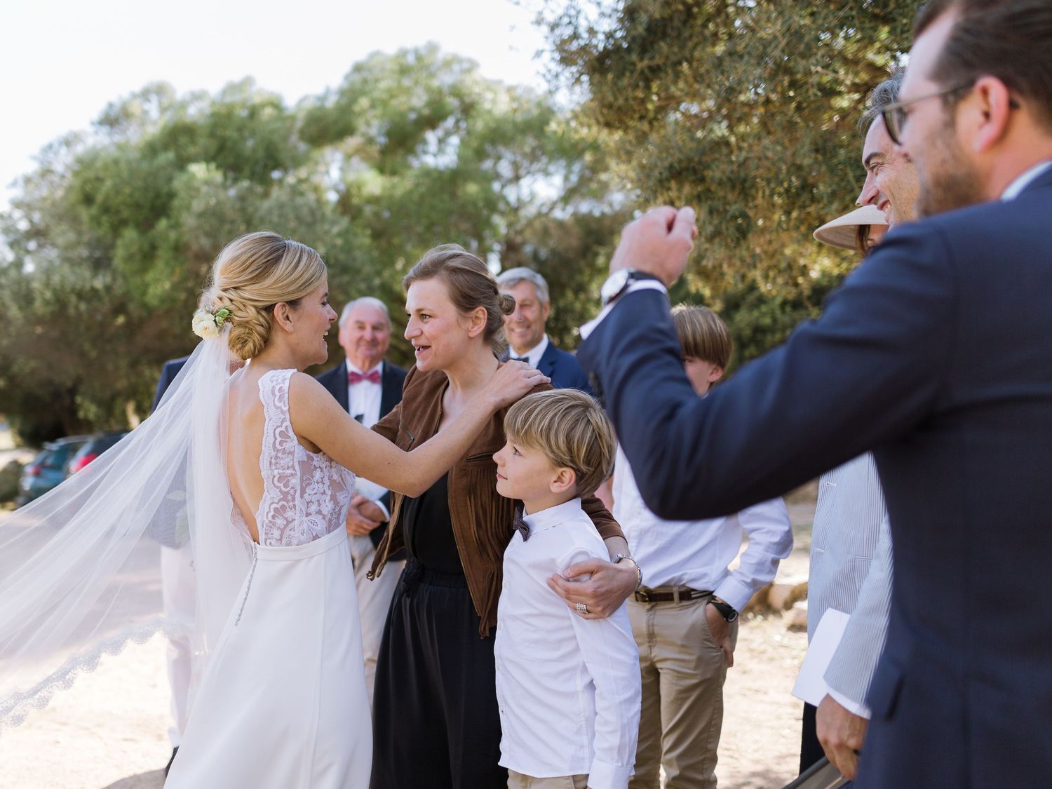 Les invités félicitent la mariée en robe blanche à l'extérieur, tandis qu'un jeune garçon et un homme immortalisent ce moment de joie.