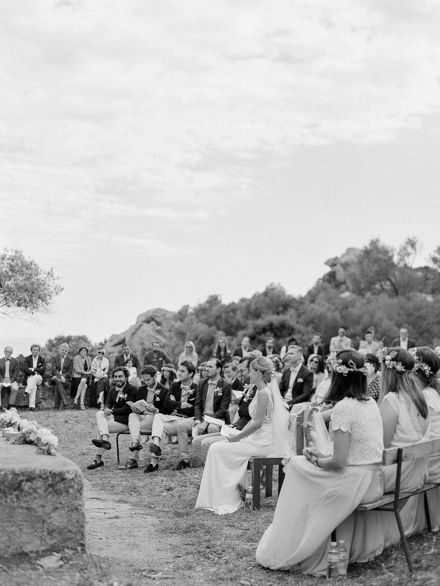 Cérémonie de mariage en plein air, en noir et blanc, avec les invités assis sur des bancs, à la trinité de Bonifacio en corse