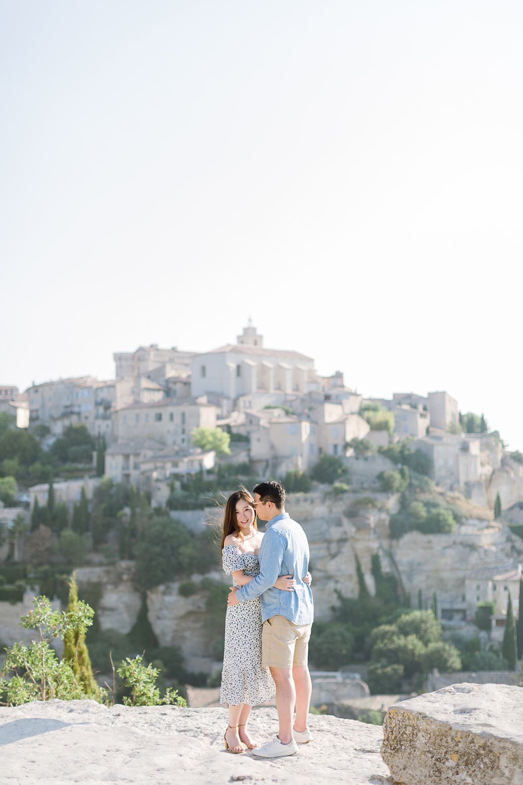 Un couple échange un tendre baiser sur un promontoire rocheux surplombant le pittoresque village perché de Gordes, en France.