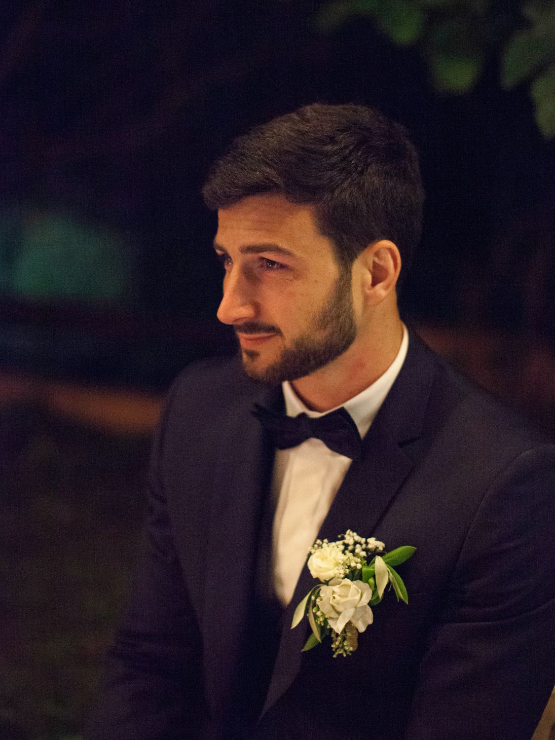 Un marié élégant en smoking noir, nœud papillon et boutonnière de rose blanche, lors d'une cérémonie de mariage en soirée à Corte