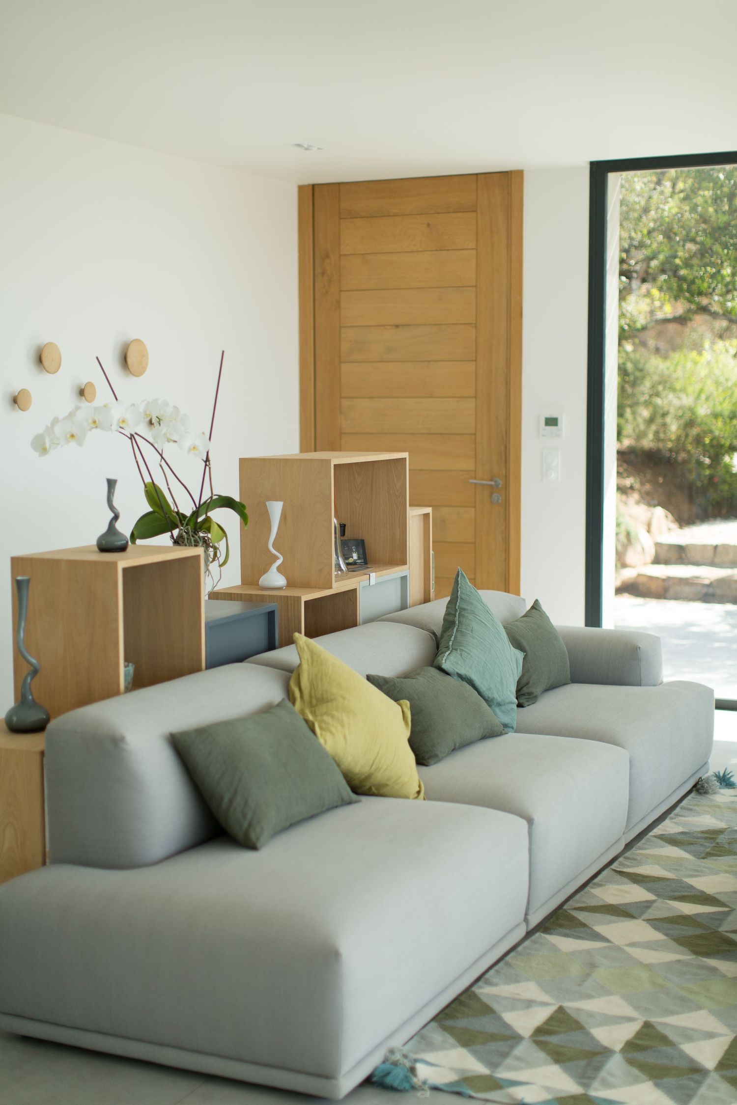 Salon de style scandinave avec canapé modulable gris et coussins pastel, étagères en bois et porte naturelle.