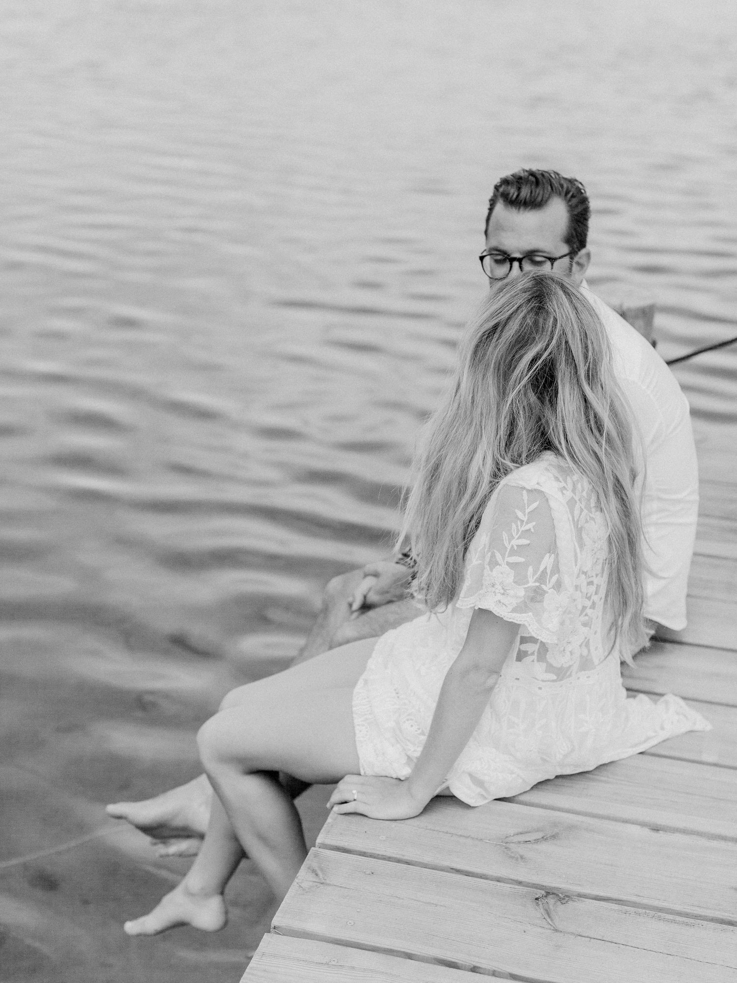 Photo en noir et blanc d'un couple assis sur un quai au bord de l'eau, les cheveux de la femme flottant au vent au Maora Beach Bonifacio.