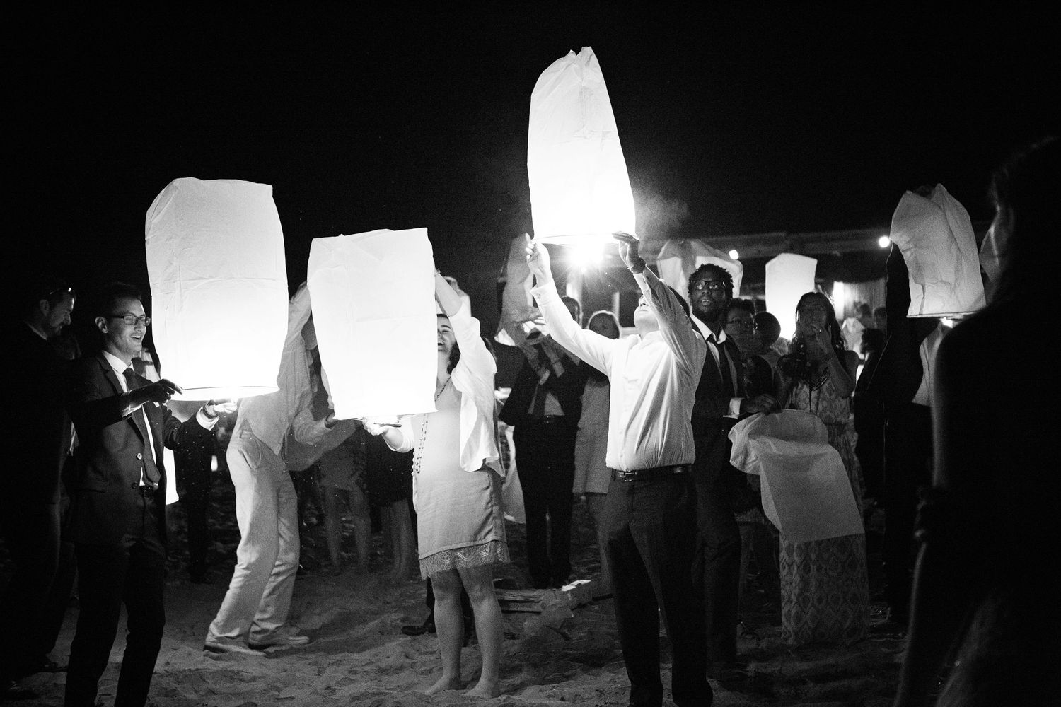 Photo en noir et blanc d'invités lâchant des lanternes célestes illuminées dans le ciel nocturne lors d'un mariage à Capo di feno à Ajaccio
