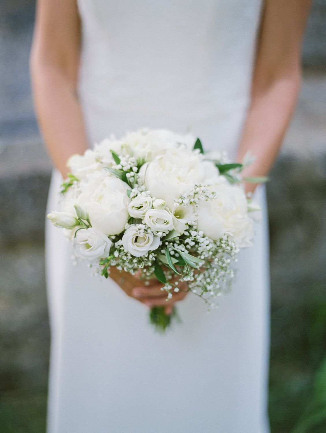 Bride holding a classic white wedding bouquet featuring peonies, roses, and baby's breath in an elegant arrangement.