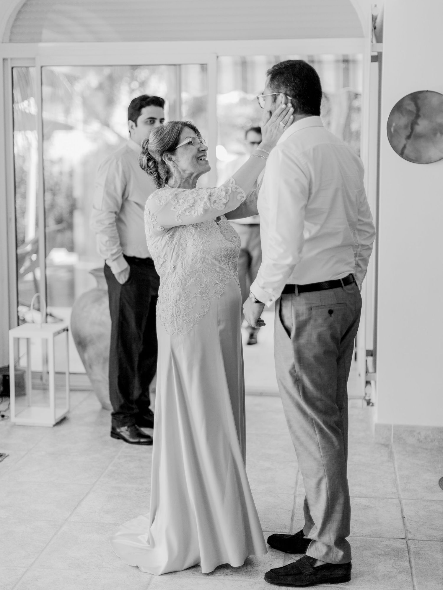 Photo en noir et blanc d'une femme en robe de soirée touchant tendrement le visage d'un homme lors d'une fête de mariage.
