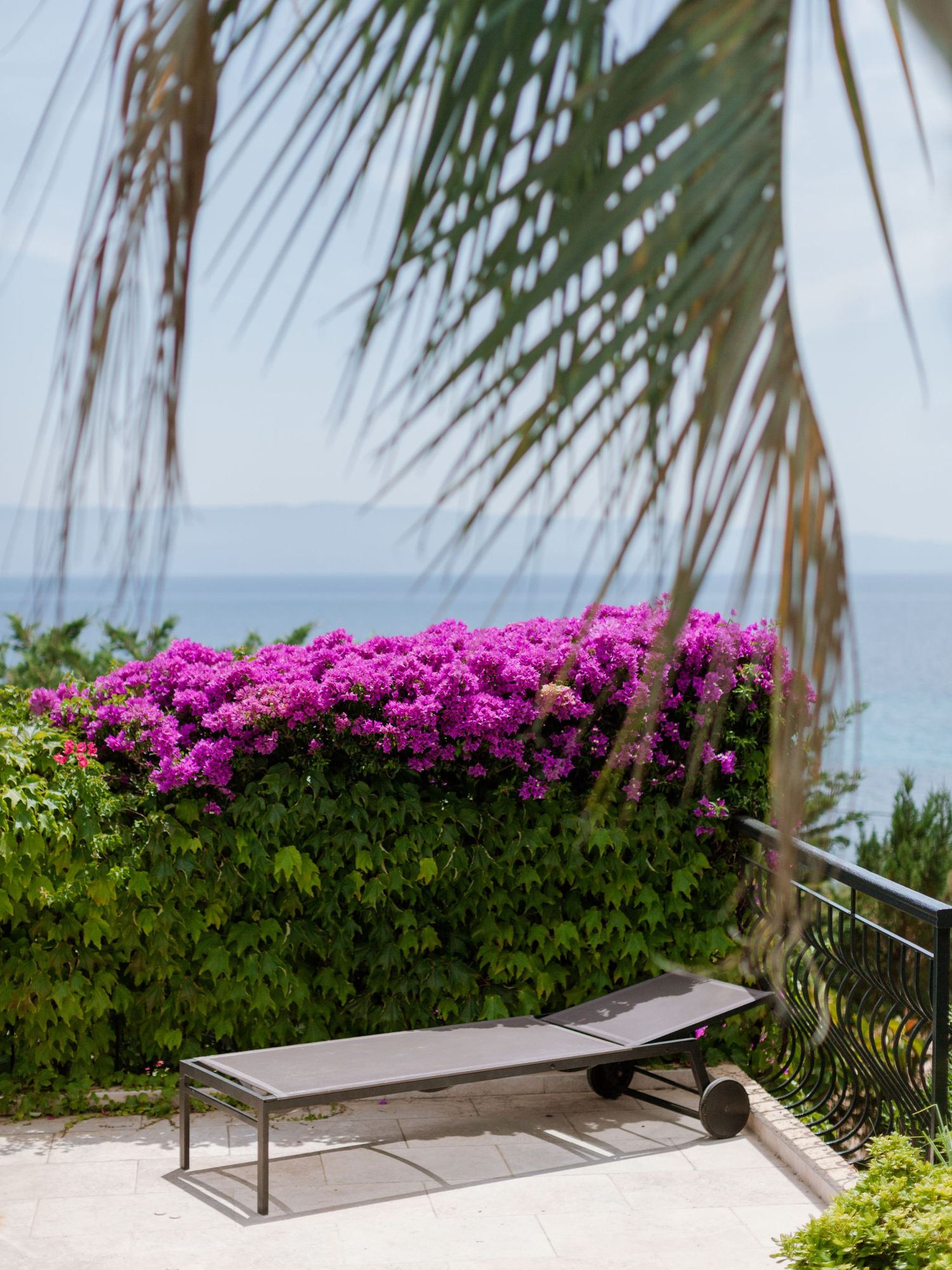 Une chaise longue près de bougainvilliers d'un rose éclatant, avec vue sur l'océan et encadrée par des palmes tropicales.