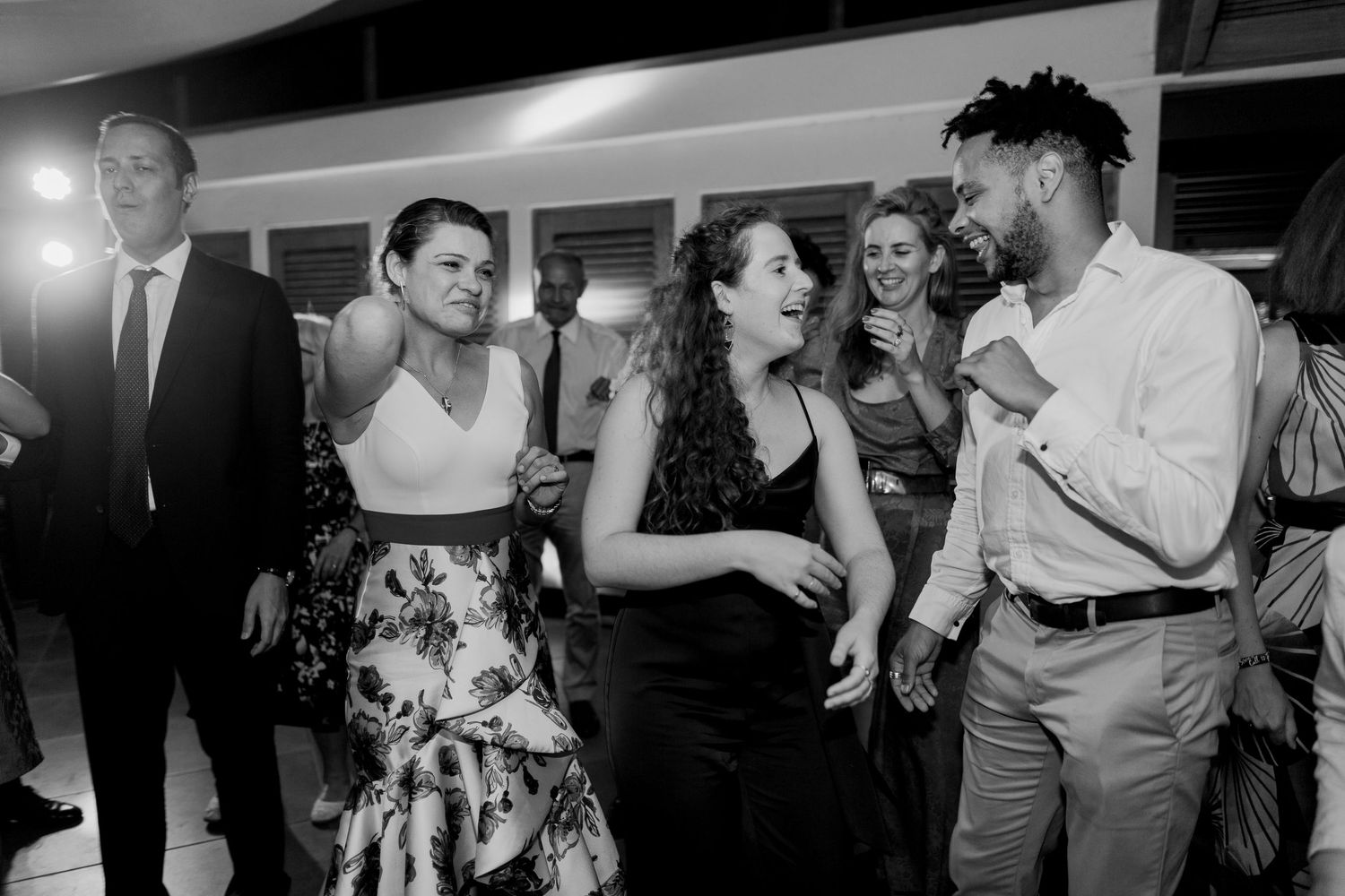Photo en noir et blanc d'invités riant et dansant ensemble lors d'une réception de mariage animée.