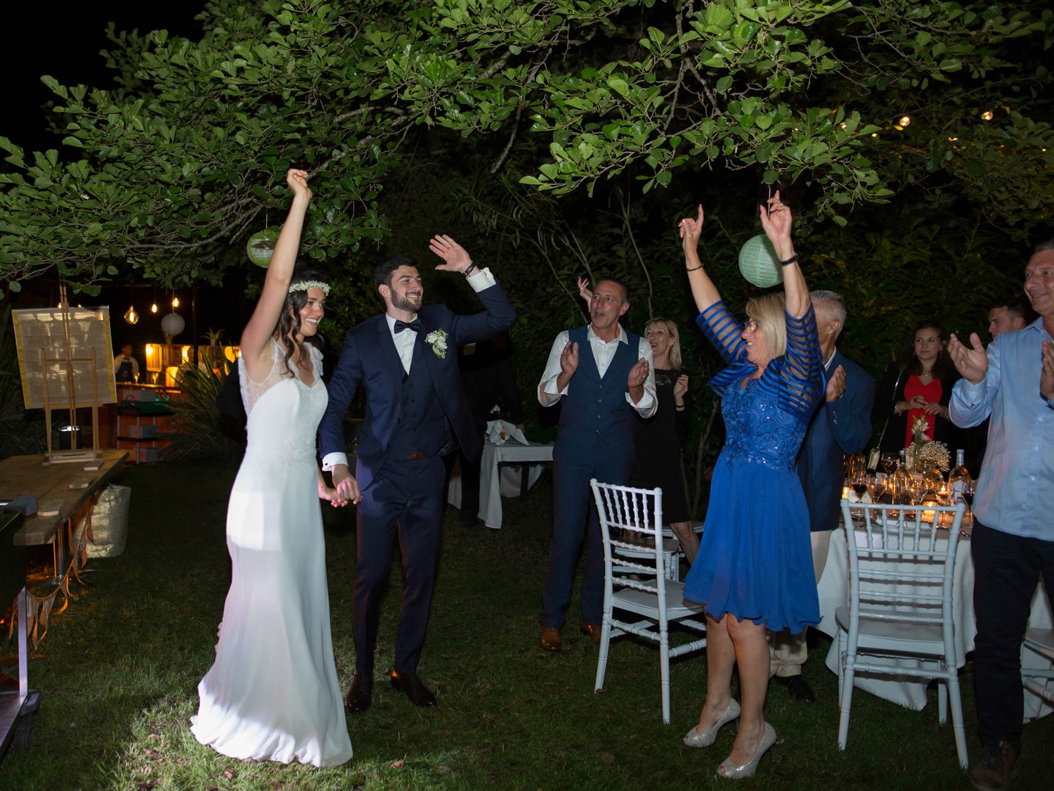 Les mariés célèbrent leur union les bras levés lors de la réception de mariage en plein air, en soirée.