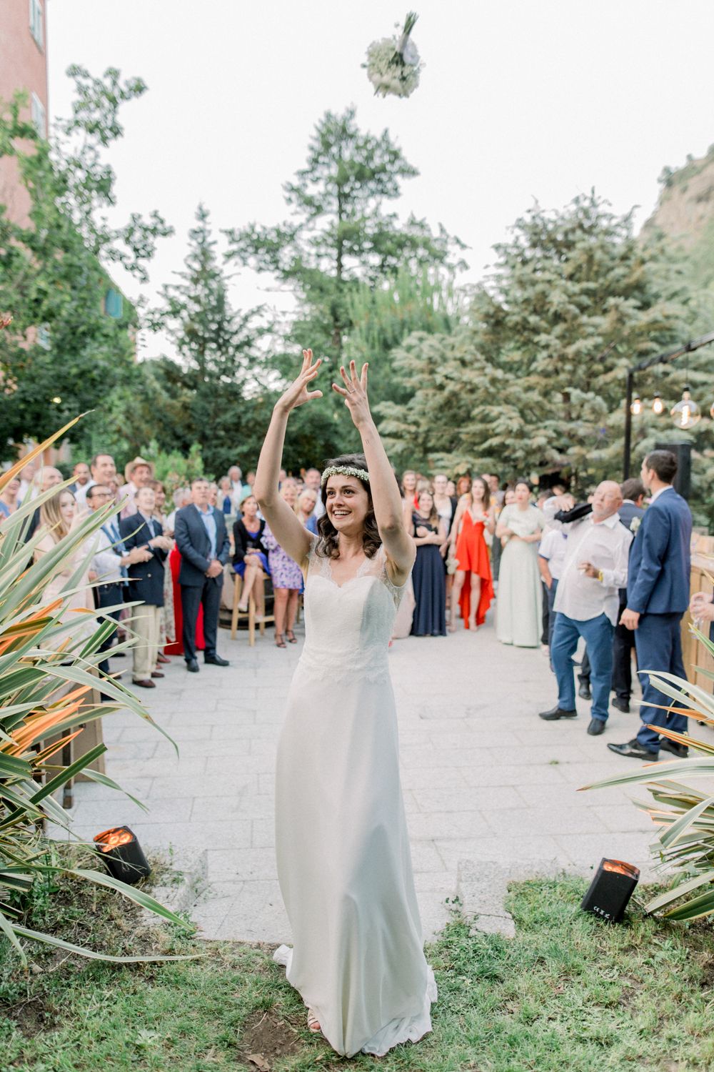 La mariée en robe blanche lance son bouquet aux invités lors de la réception de mariage en plein air à la restonica Corte