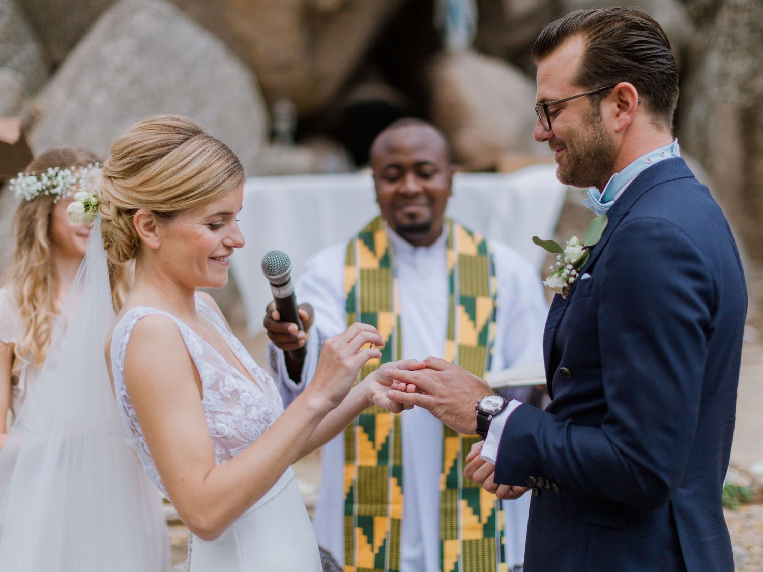 La mariée passe l'alliance au doigt du marié lors d'une cérémonie en plein air, sous le regard souriant de l'officiant