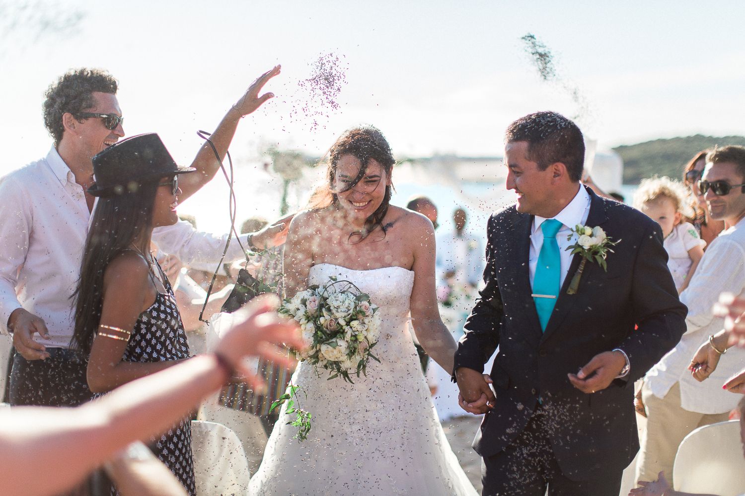Les mariés traversent une pluie de confettis lors d'une cérémonie de mariage en plein air sur la plage, entourés de leurs invités.