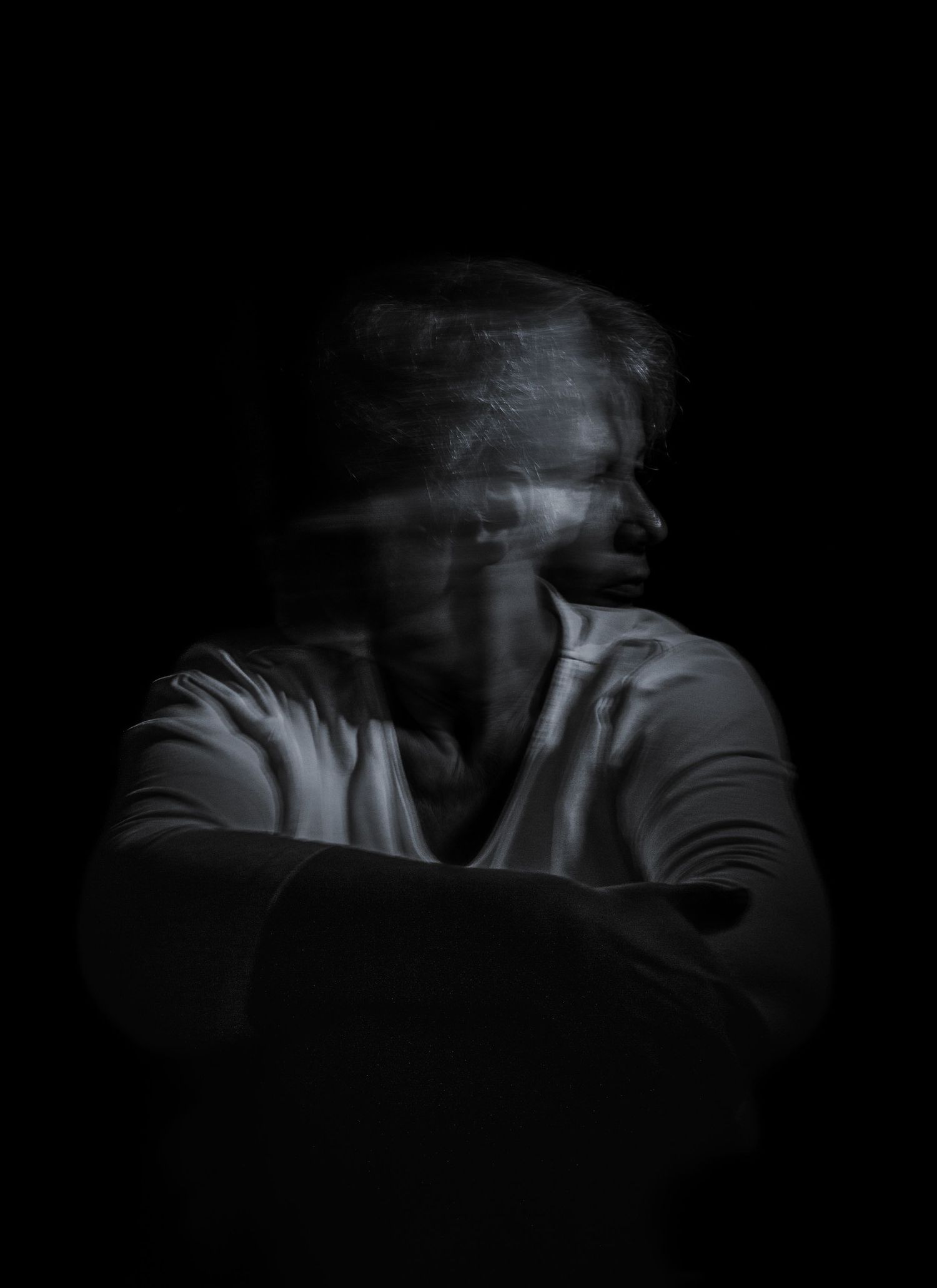 Un portrait fantomatique en pose longue d'une personne en chemise blanche avec un effet de flou de mouvement sur fond noir.