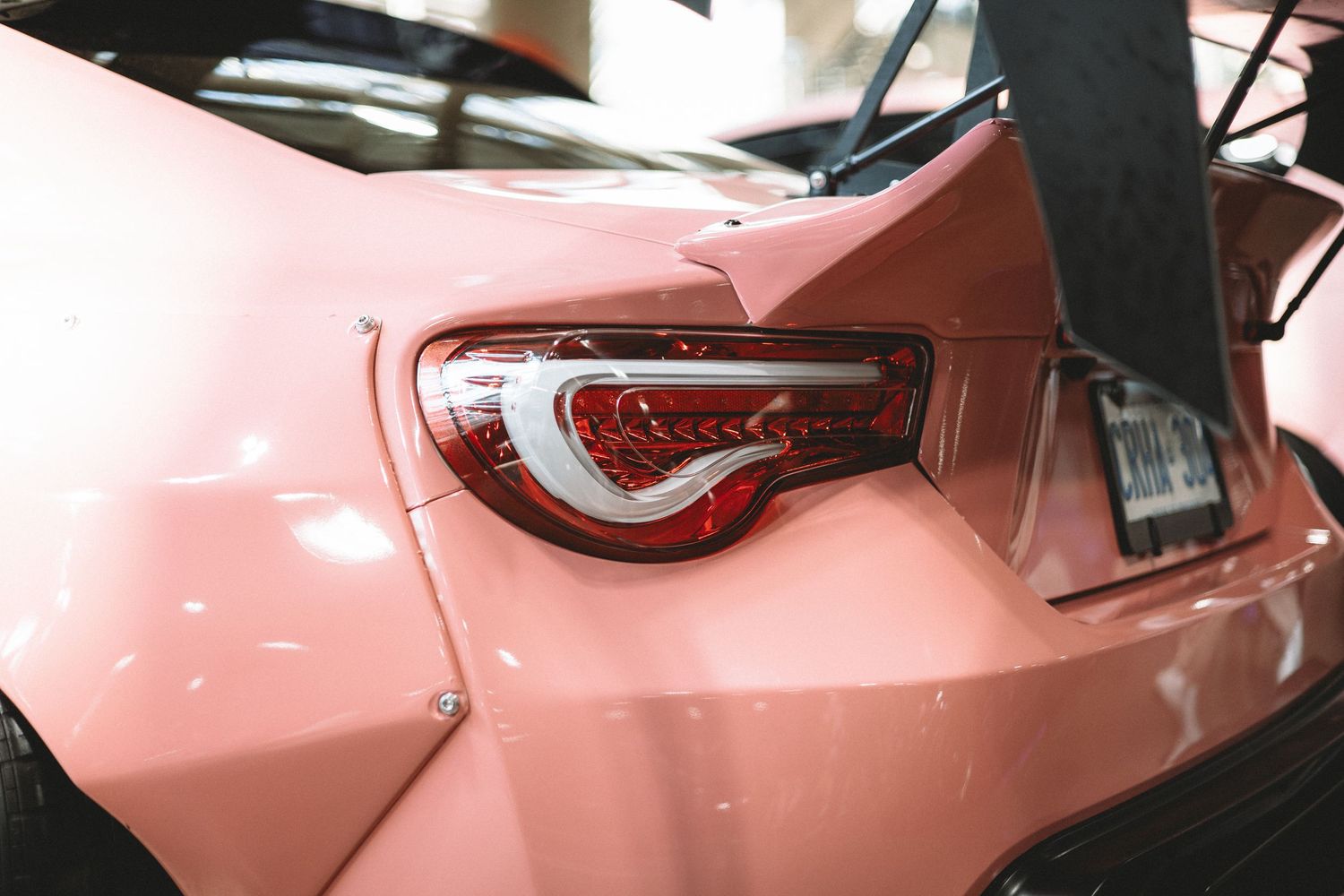 Close-up of the rear of a pink sports car showing the taillight and a large rear wing attached to the trunk.