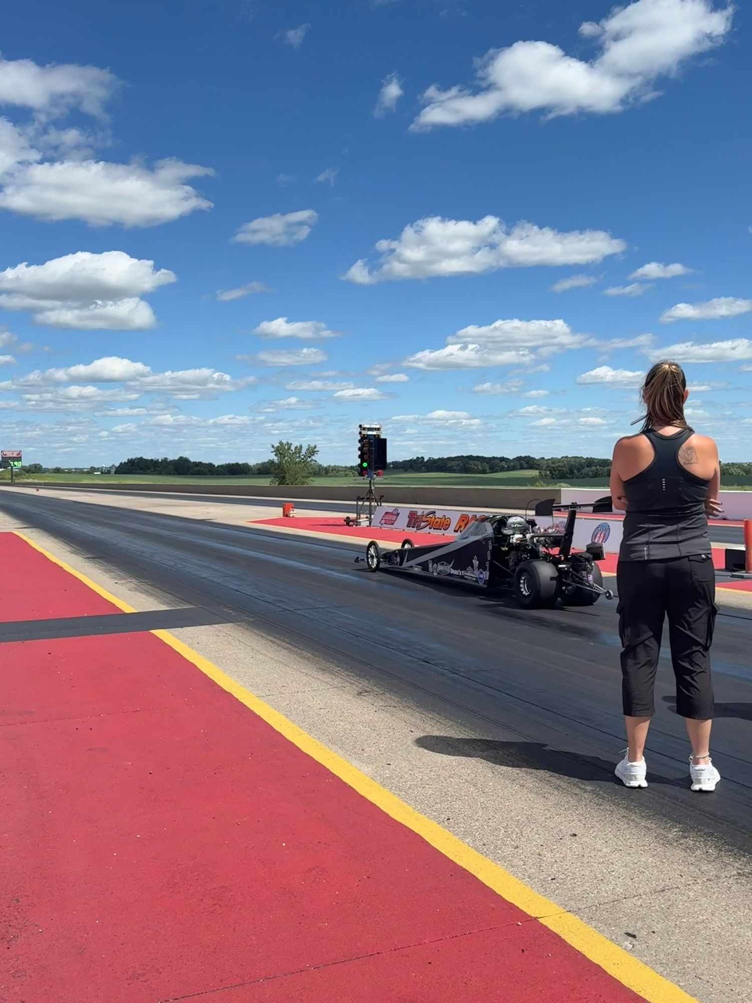 Morgan watching drag racing car of her son on sunny racetrack in Iowa.