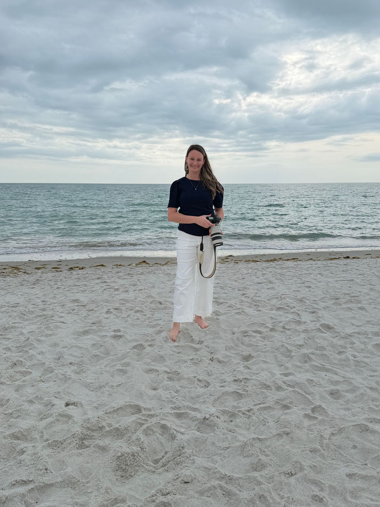Morgan standing on beach holding a camera, representing her branding, marketing, and design services for small business owners in Owatonna