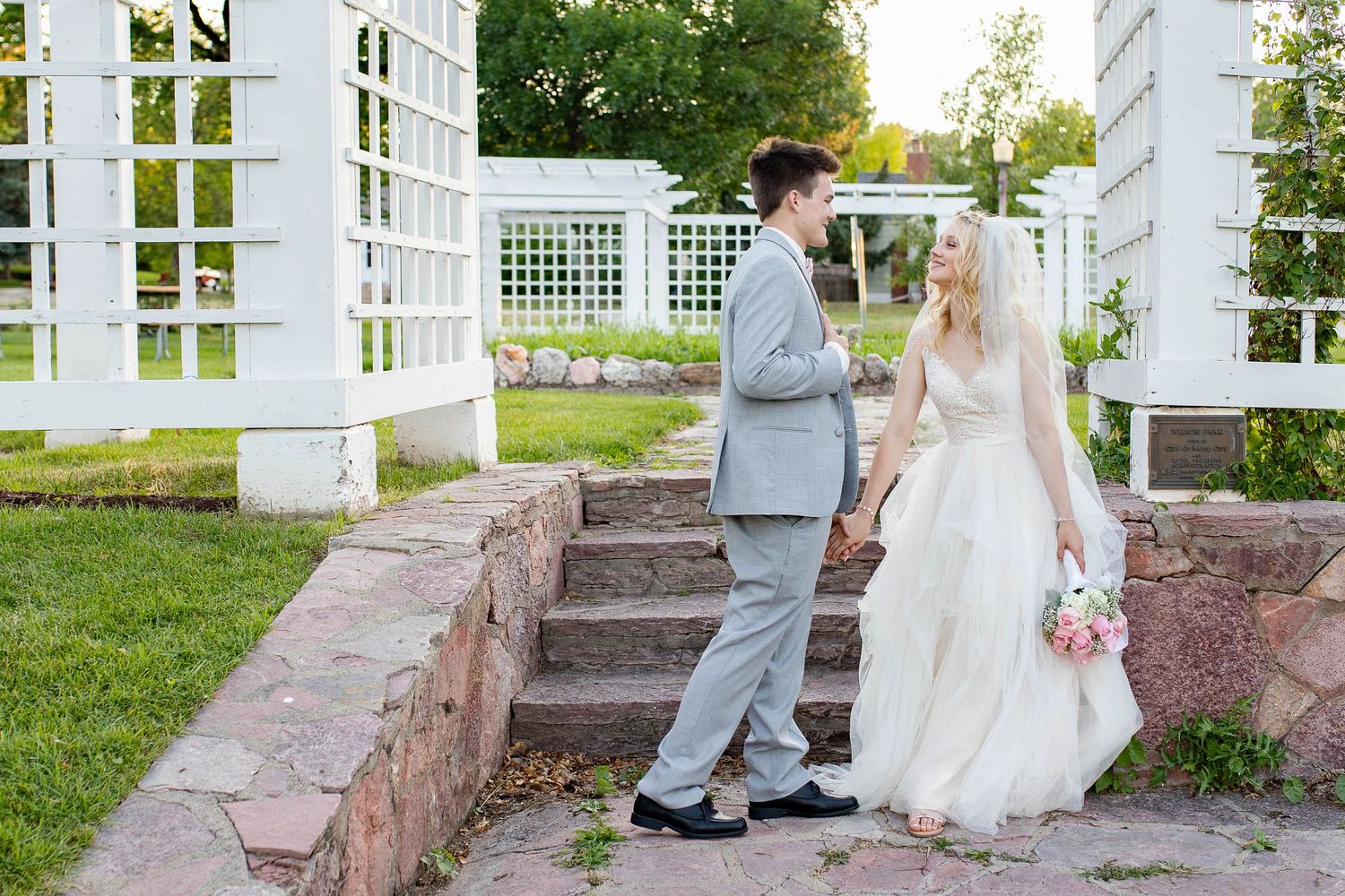 Bride and groom walking on stone steps in a white pergola garden setting on their wedding day.