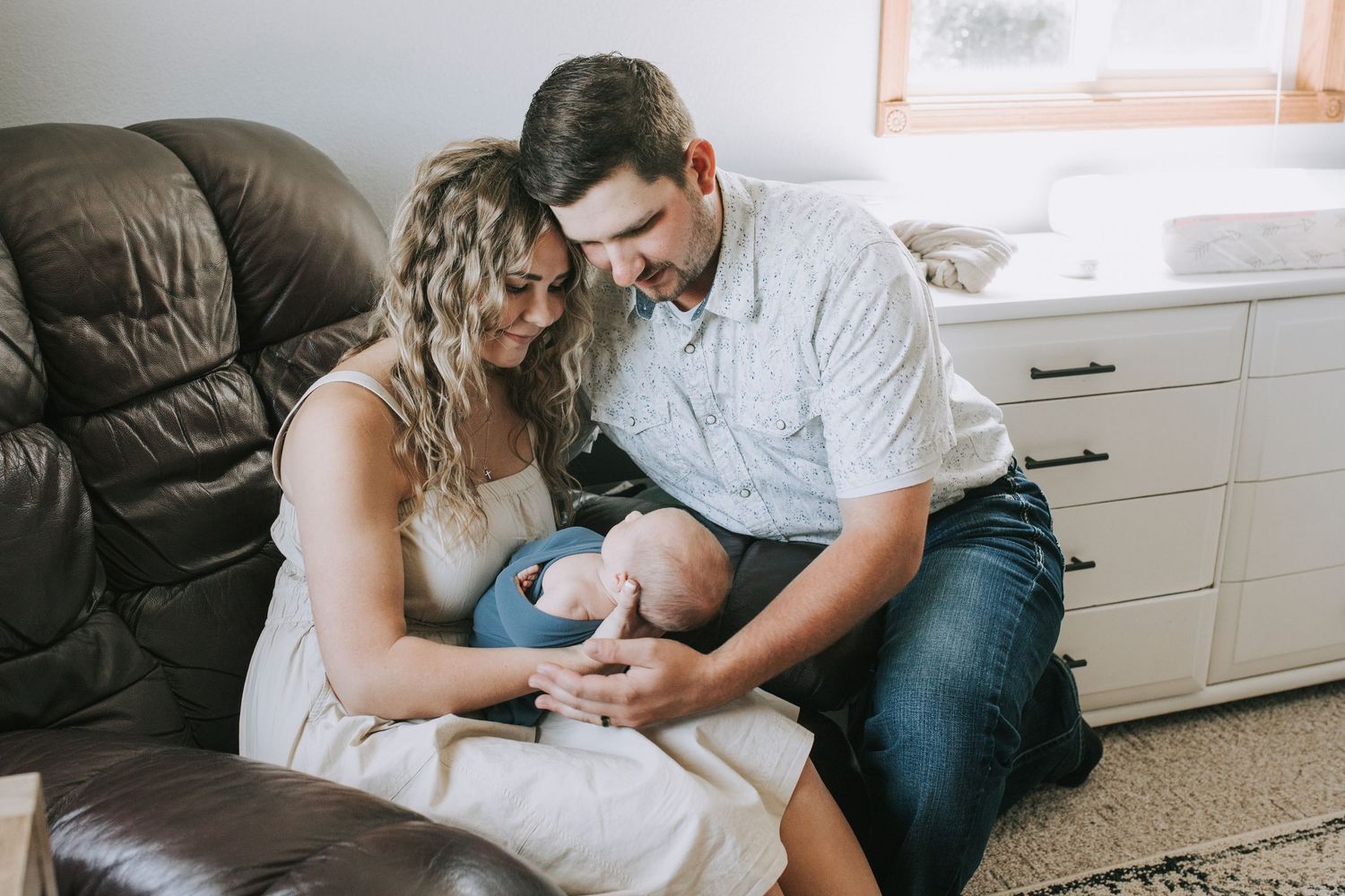 Happy couple sitting on floor smiling down at their newborn baby in a cozy home.