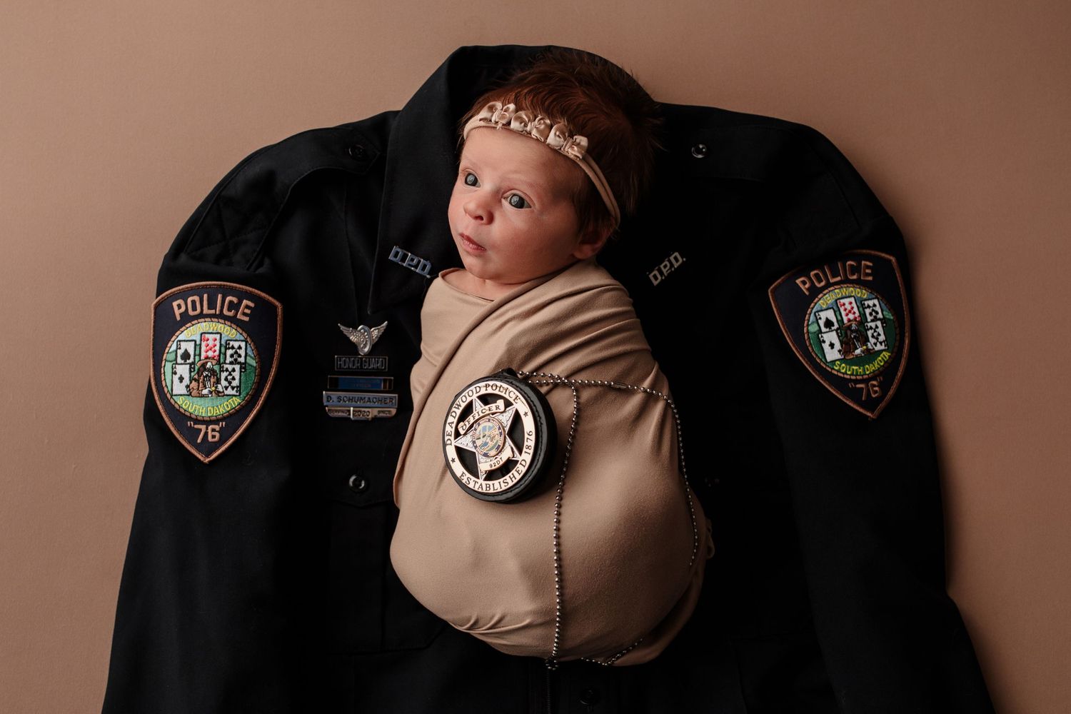 Swaddled newborn baby girl resting on a police uniform jacket with badge and patches.