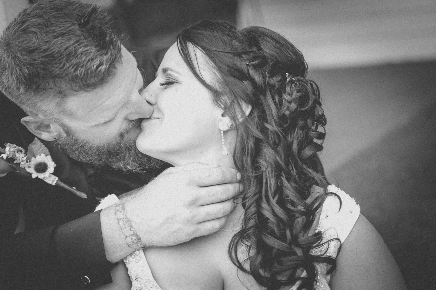 Black and white wedding photo of groom kissing bride on cheek, bride wearing elegant updo hairstyle.