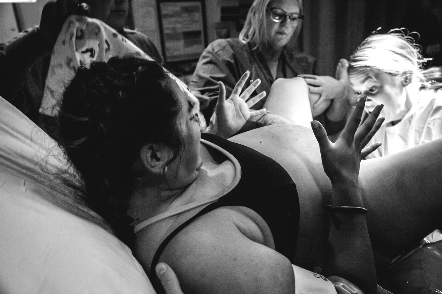 Black and white photo of a woman during active labor assisted by medical staff in delivery room.