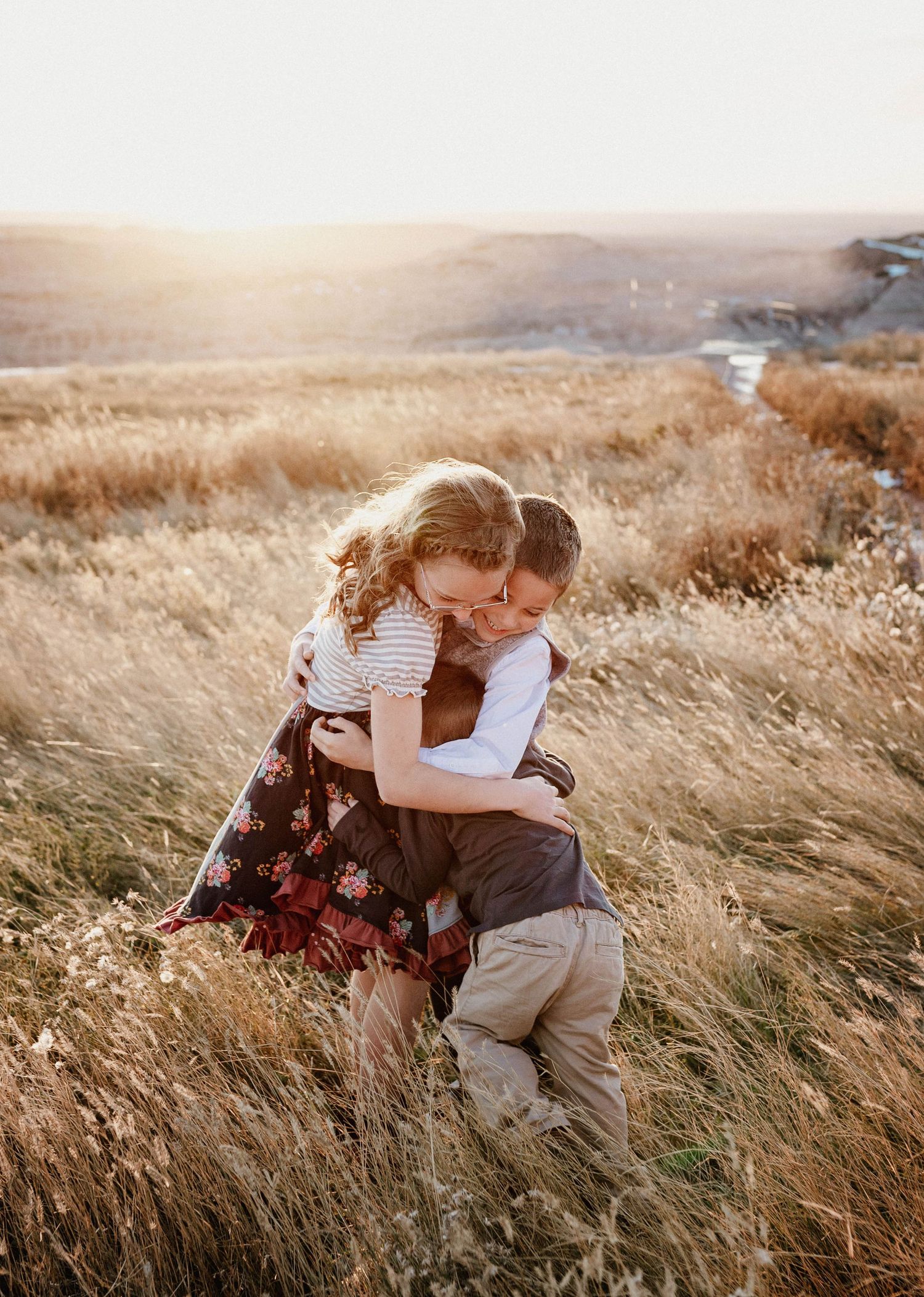 Woman and child sharing a warm hug in a sunlit golden grass field at sunset.