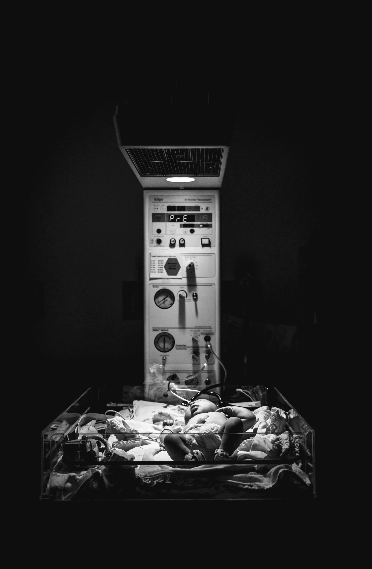 Newborn baby resting under a hospital warming station with medical equipment in dark background.