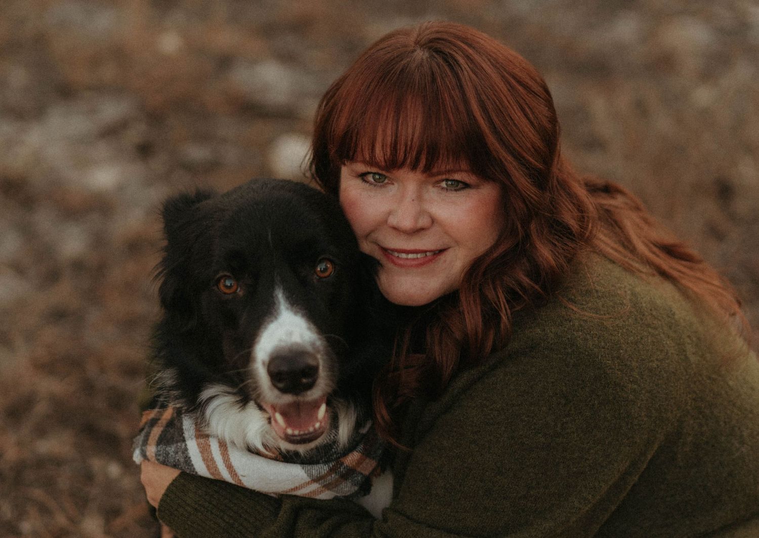 Smiling redhead woman hugging a happy black and white Border Collie dog outdoors.