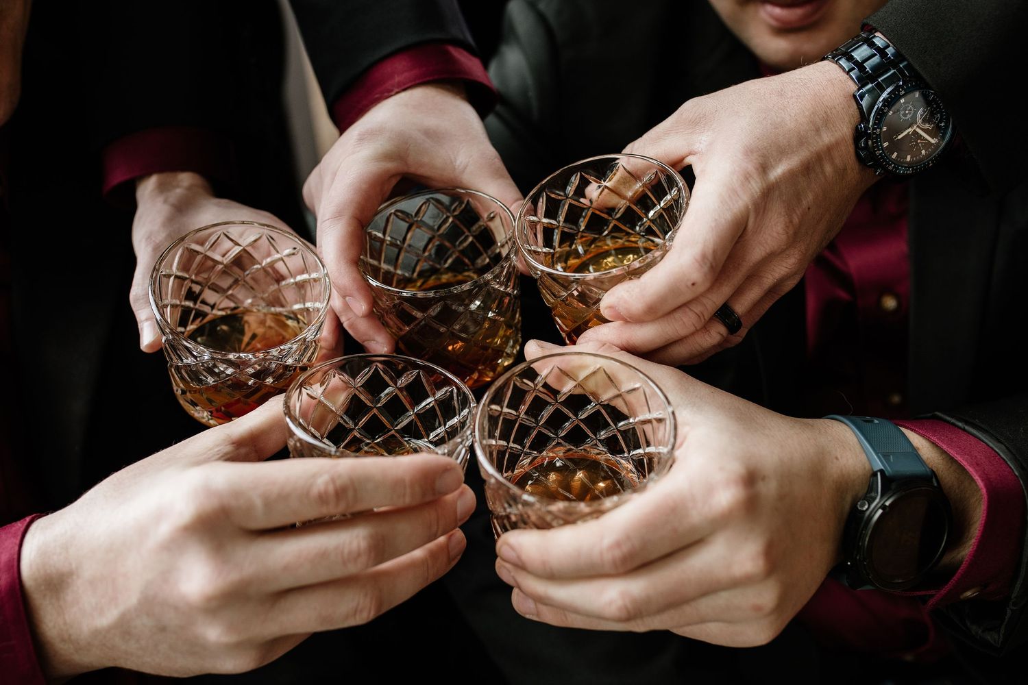 Group of men toasting with crystal whiskey glasses filled with bourbon on ice in a celebratory cheers.