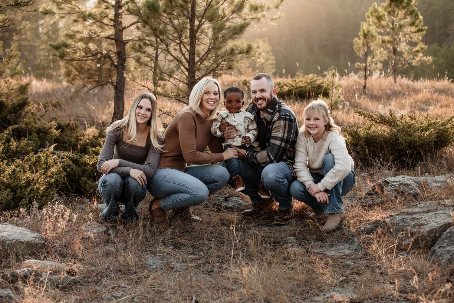 A family sitting together outdoors on rocks during golden hour with a warm autumn sunset backdrop.