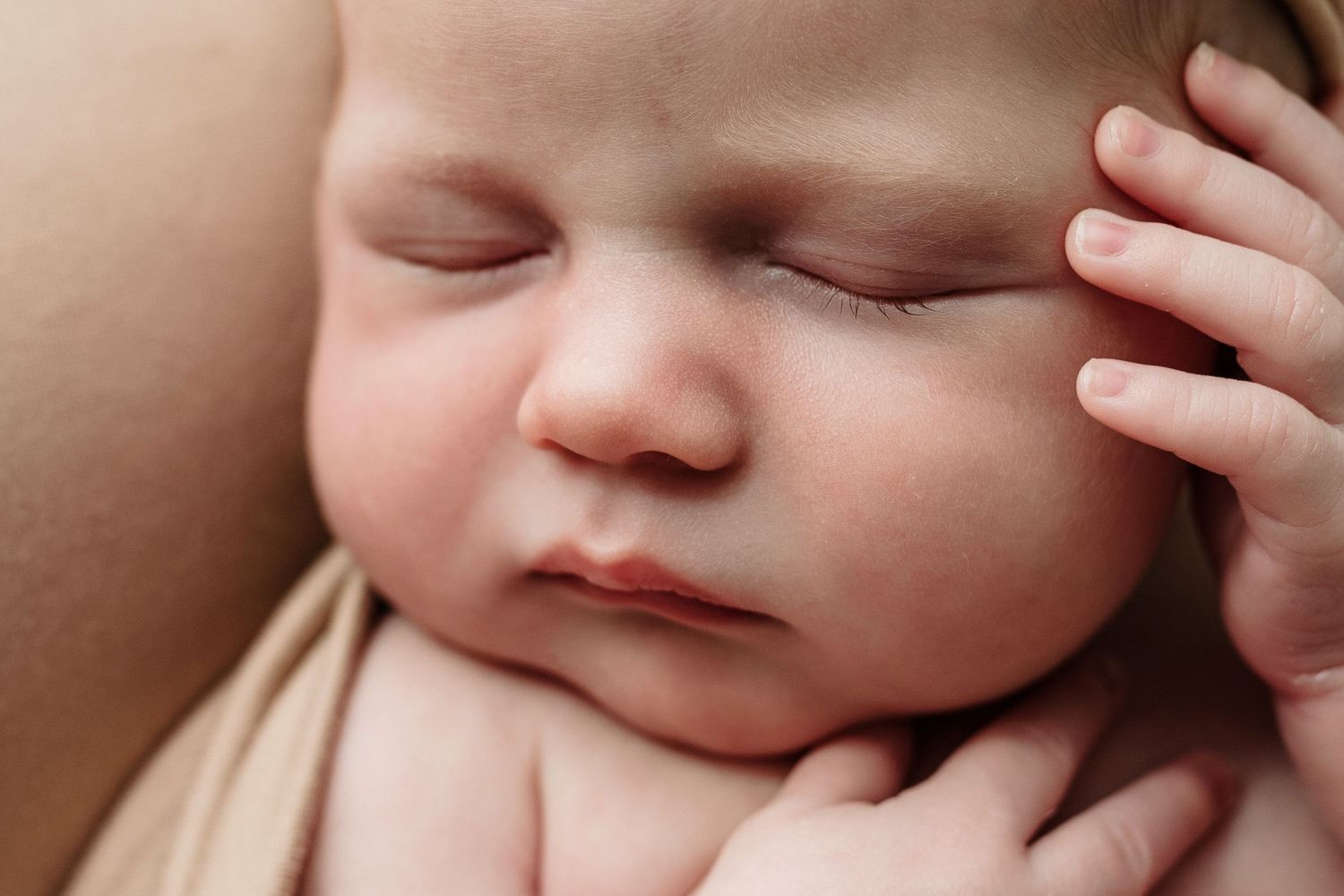 Close-up of peaceful sleeping newborn baby resting on parent shoulder with tiny hand raised.