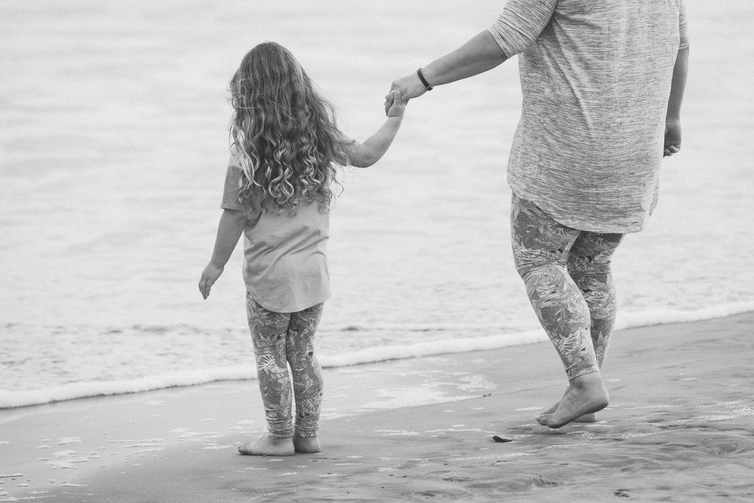 Young girl holds an adults hand while walking along the ocean shoreline.