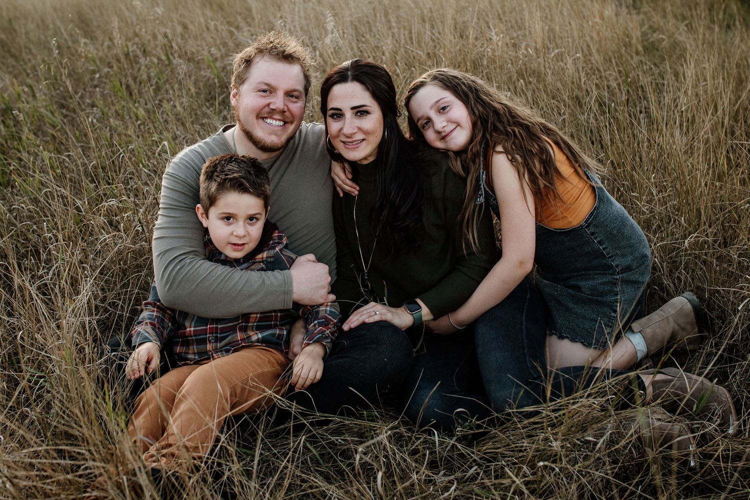 A group sits together in a rustic field of golden grass during a casual outdoor photo session at sunset.
