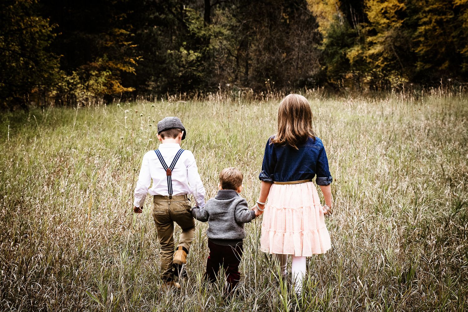 Family walking together through a rustic autumn meadow field as silhouettes in golden evening light.