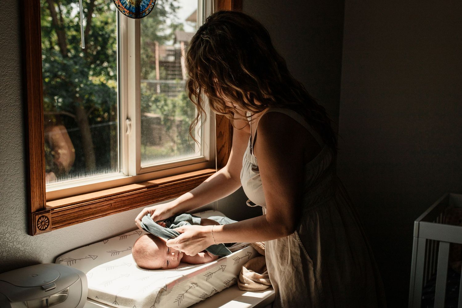 Mother tenderly caring for her newborn baby on a sunlit windowsill in a cozy nursery.