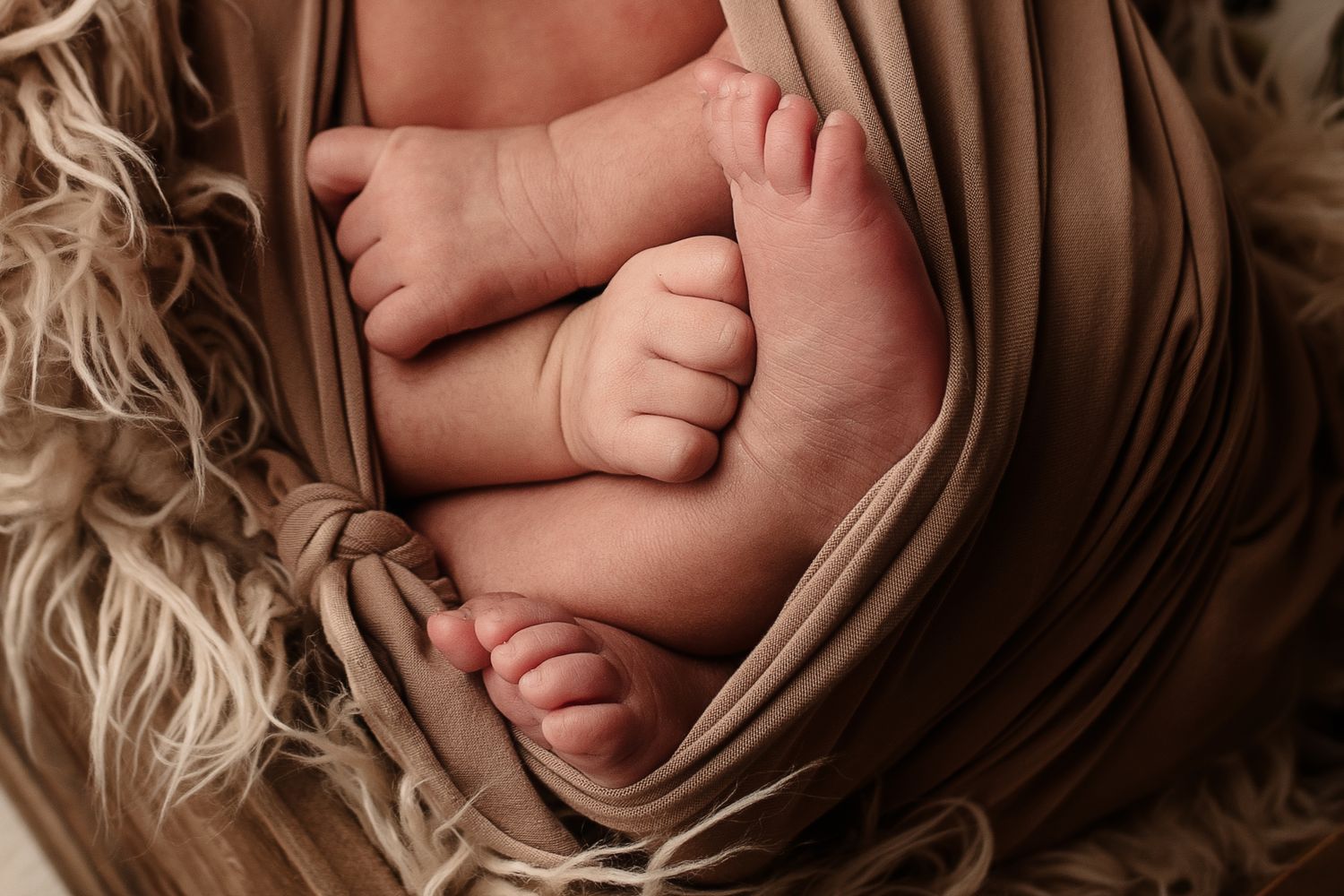 Close-up of newborn twin babies tiny feet and toes wrapped in soft beige fabric.
