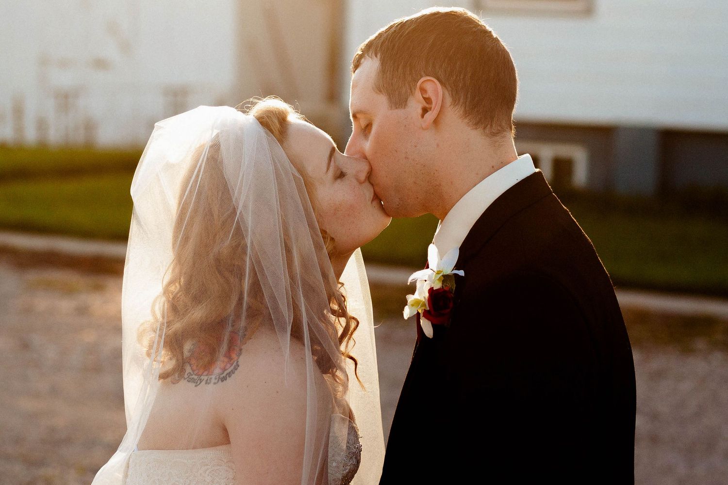 A bride and groom share a romantic kiss outdoors in golden sunset light, with the bride wearing a white veil.