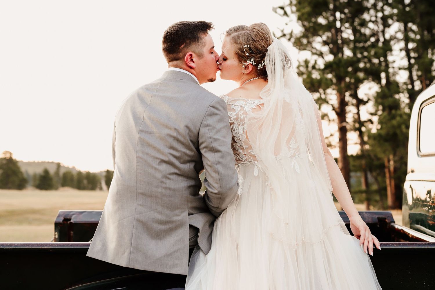 A bride and groom share a romantic kiss outdoors, with the bride wearing a white gown and veil at their wedding.