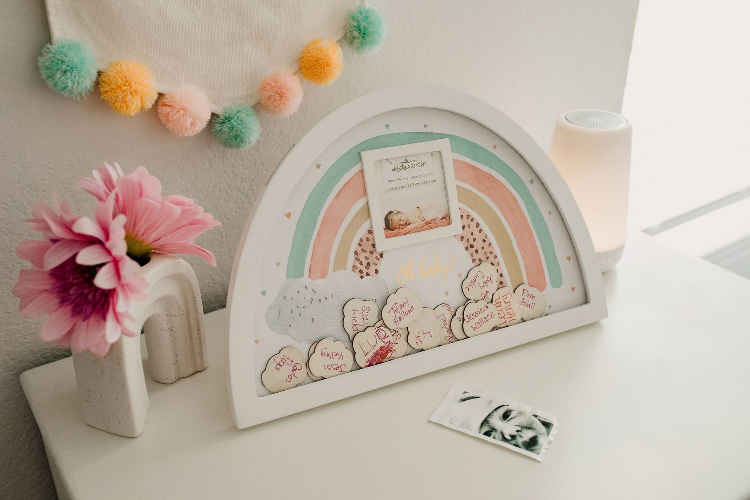 Rainbow-shaped wooden baby guest book display on white dresser in pastel nursery decor setting.