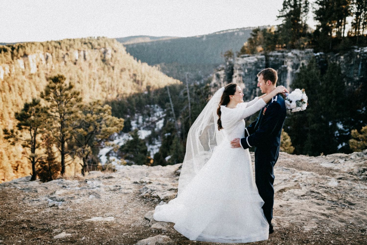 Bride and groom share a romantic moment on a rocky cliff with a stunning canyon and pine forest backdrop.